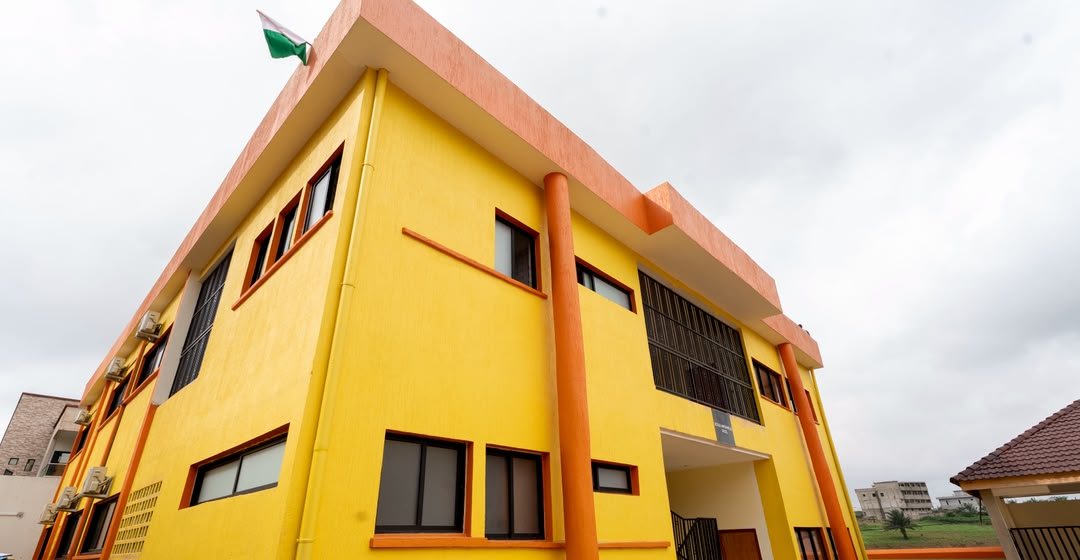 La façade jaune et orange de l'école, drapeau ivoirien hissé sur le toit